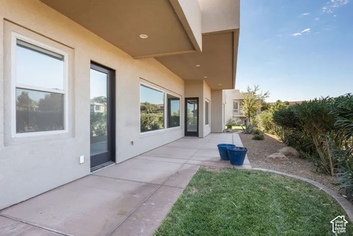 Exterior stucco finish, covered patio, multiple windows, grass area, and xeriscaped plantings