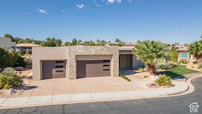 Modern architectural home featuring a three-car garage with contemporary metal-finish doors, stamped concrete driveway with curved landscaping borders, and a sophisticated stone and stucco exterior