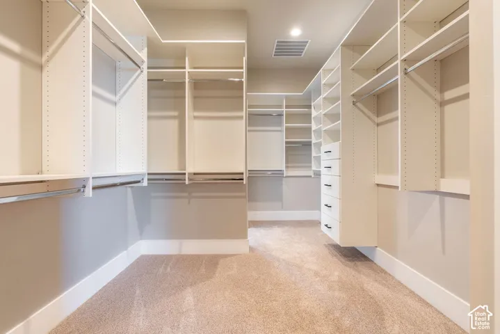 Spacious walk-in closet featuring custom white shelving and organizational systems, abundant hanging space, and neutral carpeting throughout