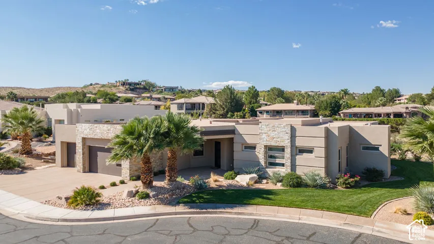 Contemporary exterior with a stucco and stone facade, integrated garage, concrete driveway, and manicured landscaping featuring mature palm trees