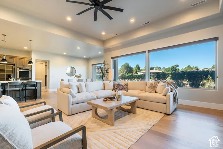 Open-concept living space featuring wood-finish flooring, tray ceilings, recessed lighting, a modern ceiling fan, and expansive floor-to-ceiling windows