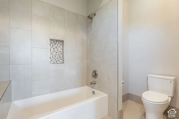 White bathtub with a built-in shower niche featuring mosaic tile