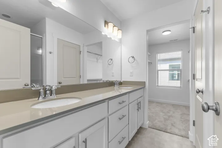 Dual-sink vanity with neutral-toned solid surface countertop, undermount sinks, white cabinetry with brushed nickel hardware, and full-width wall mirror