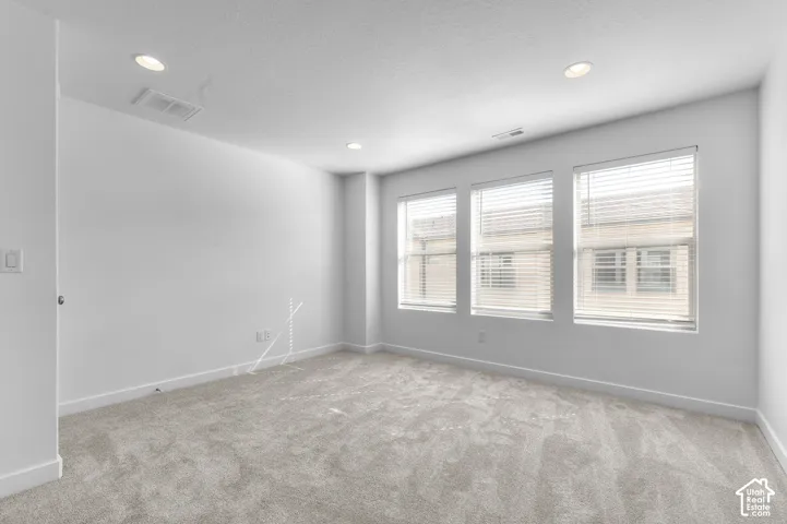 Neutral-toned carpeting, recessed ceiling lighting, and three windows featuring horizontal blinds