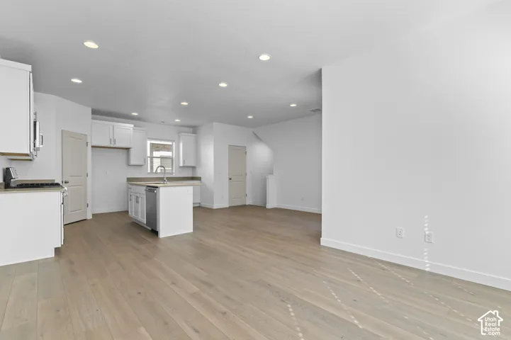 Open-concept interior featuring light wood-finish flooring, recessed lighting, white cabinetry, a kitchen island with a built-in sink, and solid-panel interior doors
