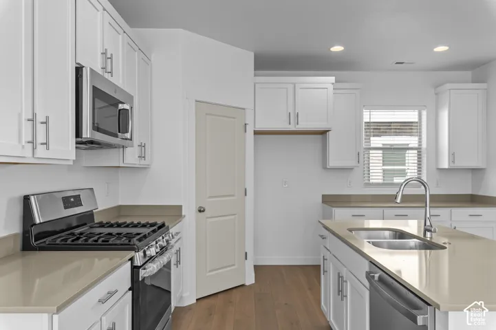 Kitchen featuring white shaker-style cabinetry, quartz countertops, a central island with an undermount dual-basin stainless steel sink, stainless steel appliances, and wood-finish flooring