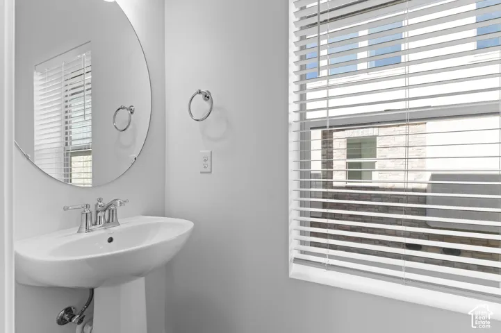 Pedestal sink featuring a polished chrome faucet, round wall-mounted mirror, and horizontal window blinds