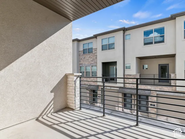 Covered balcony featuring concrete flooring, stone-veneer pillars, and a metal horizontal-bar railing