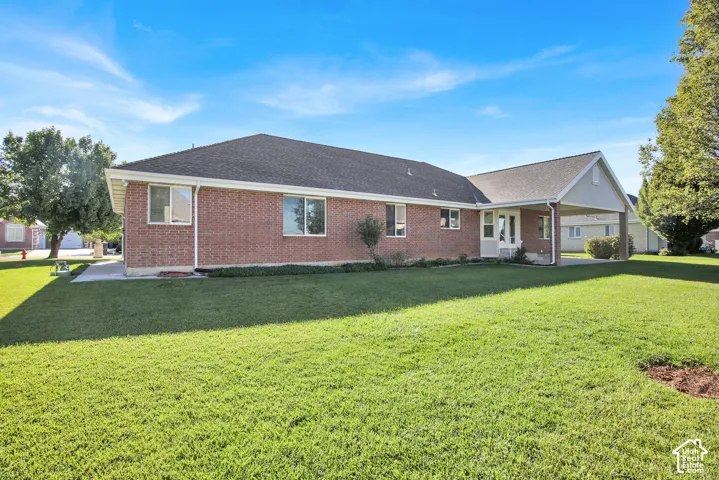 Red brick exterior featuring a hip roof, expansive lawn, covered patio, and concrete walkway