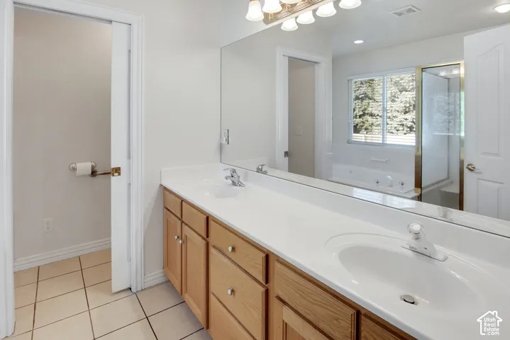 Double vanity with integrated sinks, neutral countertop, wood-finish cabinetry, full-width mirror, and tile flooring