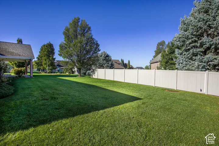 Expansive backyard featuring a manicured lawn, full-height vinyl perimeter fencing, and mature trees