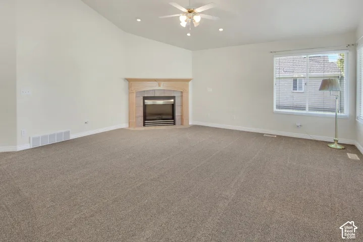 Vaulted ceiling with an integrated ceiling fan and light fixture, centered corner fireplace with a decorative mantel and stone-tile surround, and large windows