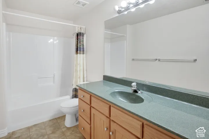 Bathroom featuring a vanity with wood-finish cabinetry, integrated solid-surface countertop with basin, wall-to-wall mirror, multi-bulb lighting fixture, and a tub-shower combination