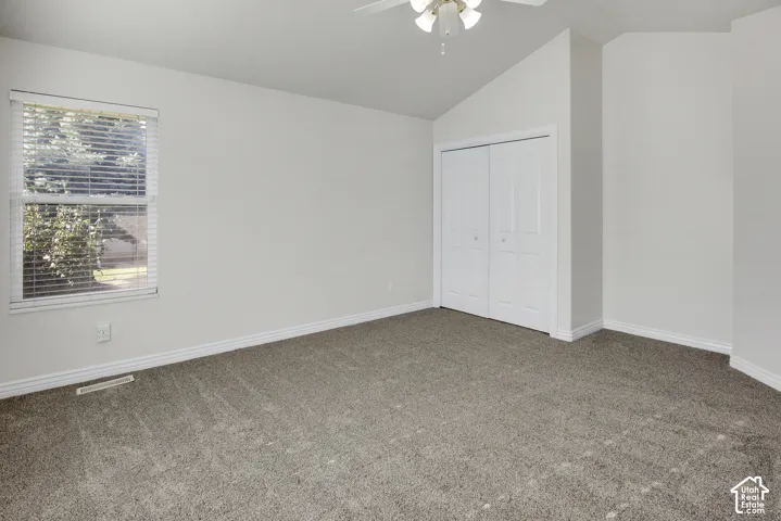 Vaulted ceiling featuring a central light fixture with an integrated ceiling fan, neutral wall paint, carpeting, and a dual-panel closet door