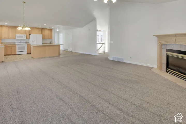 Vaulted ceilings, built-in fireplace with tiled surround, light-toned cabinetry, kitchen island, and recessed lighting