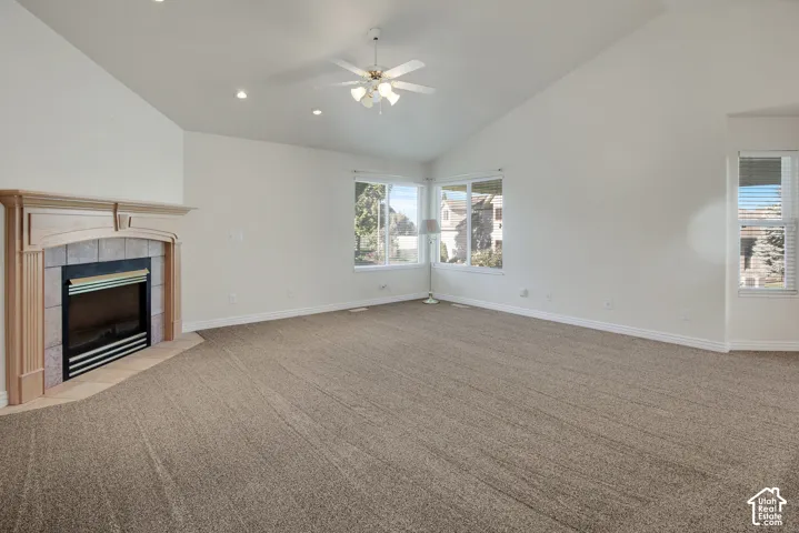 Vaulted ceilings, fireplace with an ornate wood mantle and tiled surround, ceiling fan with integrated lighting, and multiple windows