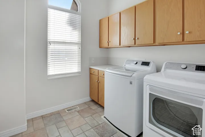Laundry room featuring natural wood-finish cabinetry, stone-style tile flooring, arched window with horizontal blinds, and solid-surface countertop space
