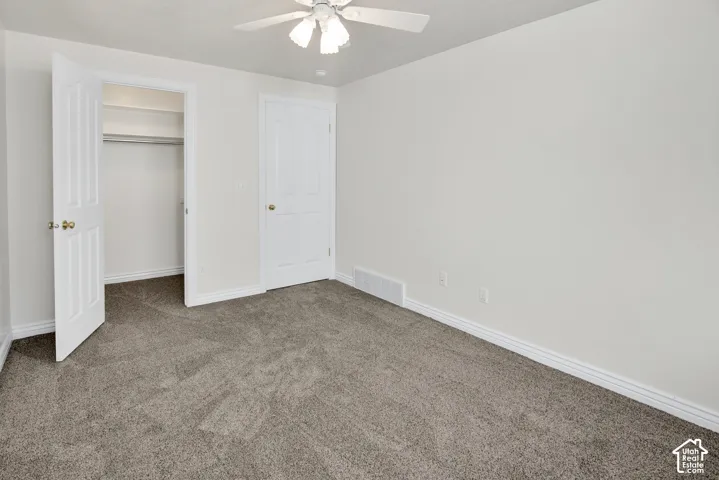Neutral-toned wall-to-wall carpeting, ceiling fan with integrated lighting, and built-in closet with shelving
