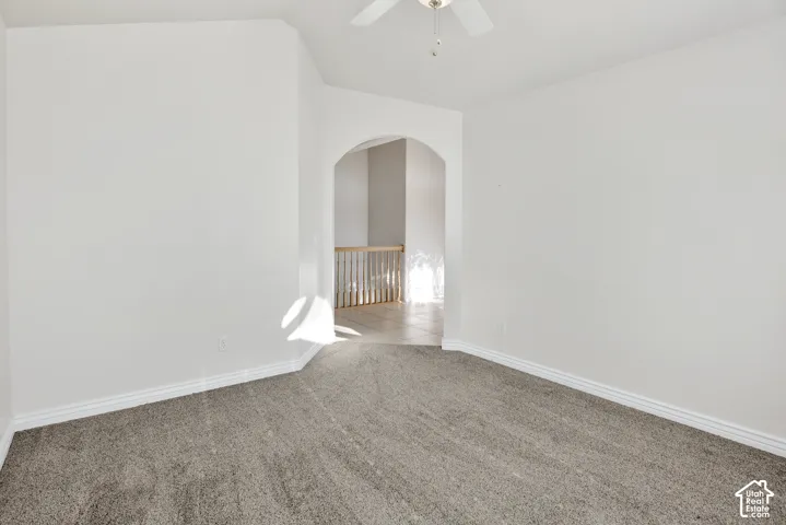 Neutral-toned room featuring a vaulted ceiling, ceiling fan, carpeting, and an arched doorway with a wooden railing