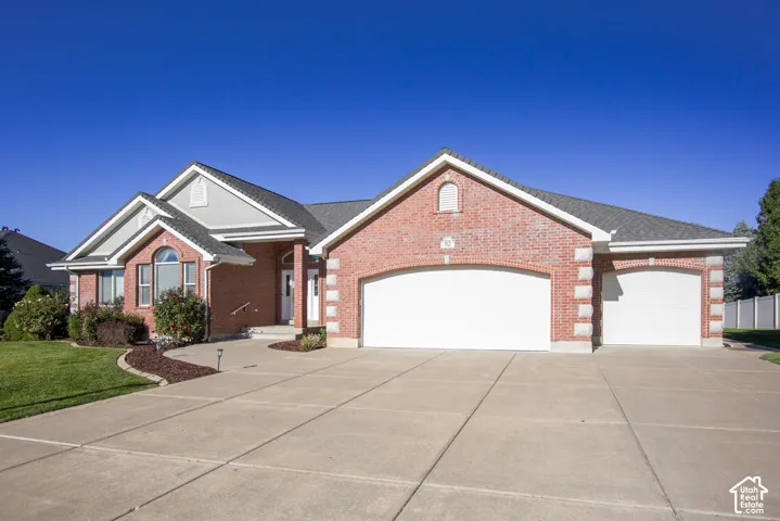 Brick Colonial home showcasing a expansive concrete driveway with three-car garage, manicured landscaping with mature plantings, arched architectural detailing, and white trim accents complementing the rich brick exterior