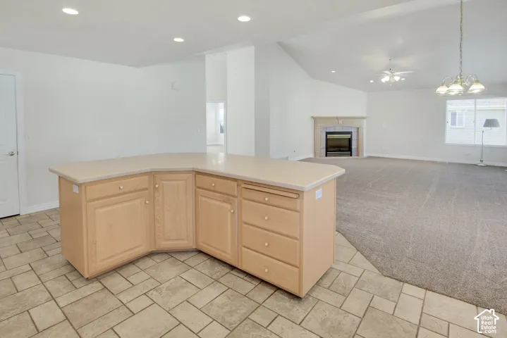 L-shaped kitchen island with neutral-toned countertops, vaulted ceilings, recessed lighting, neutral carpeting, and a fireplace with a stone surround