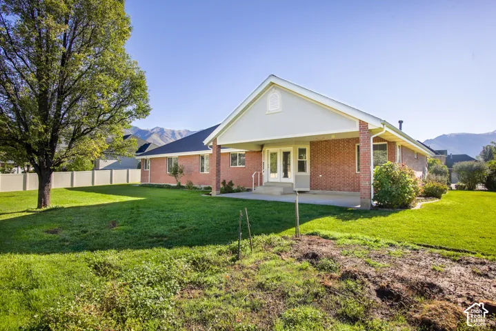 Brick exterior with a covered rear patio, expansive lawn, mature tree, and mountain backdrop