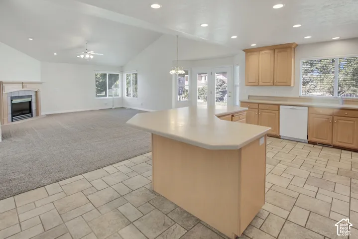 Open floor plan featuring vaulted ceilings, recessed lighting, a center kitchen island with a neutral countertop, and a fireplace with a decorative mantel