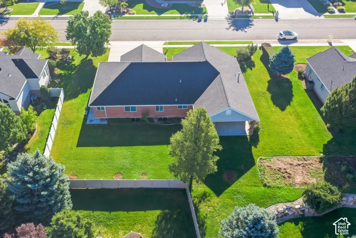 Aerial perspective featuring a brick-exterior residence, a multi-car garage, an expansive lawn, established trees, and perimeter fencing