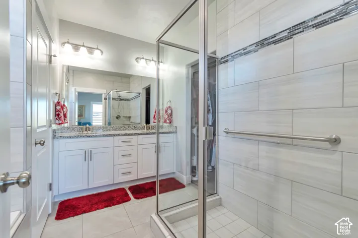 White shaker-style cabinetry with stone-finish countertops, glass-enclosed shower with horizontally tiled walls and decorative inlay, and dual-light vanity fixtures