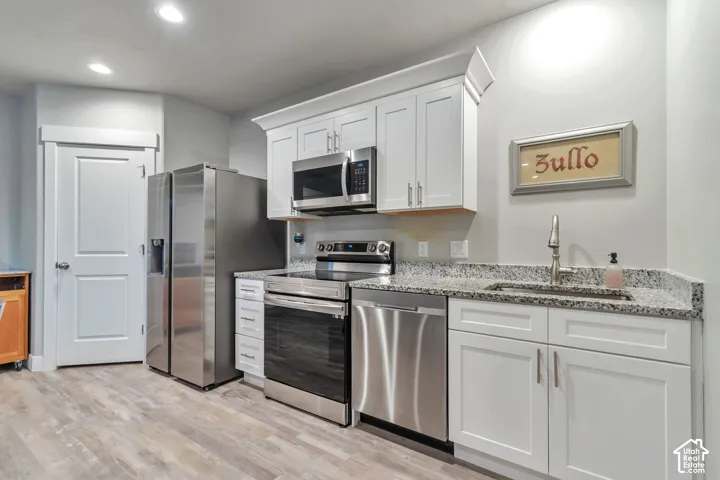 White shaker-style cabinetry with crown molding, stone-patterned countertops, stainless steel appliances, and wood-finish flooring