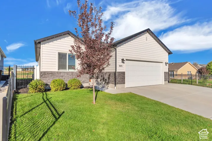 Single-story exterior featuring horizontal siding, stone veneer accents, a concrete driveway, a two-car garage, and metal perimeter fencing
