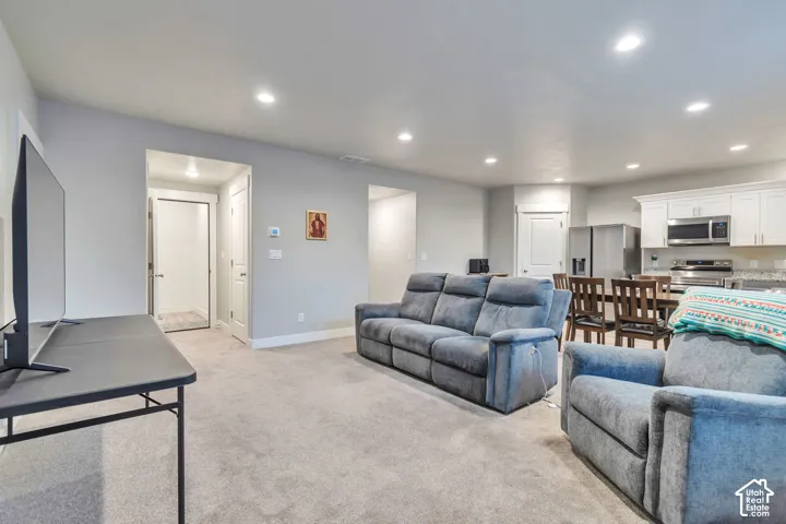 Open-concept interior featuring recessed lighting, neutral wall tones, wall-to-wall carpeting, and white shaker-style cabinetry with stone-surface countertops