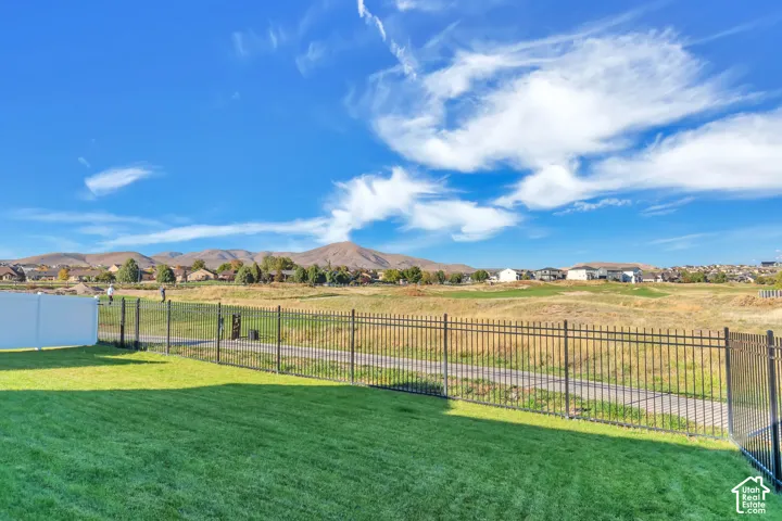 Manicured lawn enclosed by a black metal perimeter fence, featuring a white vinyl privacy partition and a backdrop of mountain scenery