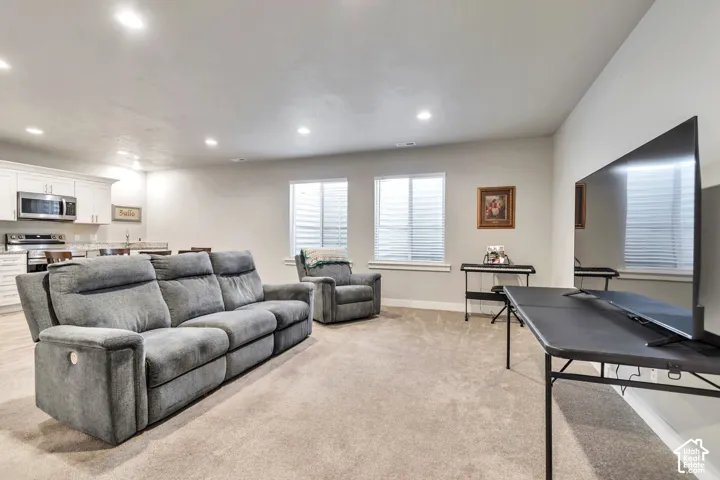 Open-concept living space featuring recessed lighting, plush wall-to-wall carpeting, two multi-pane windows, and white cabinetry in the kitchen area