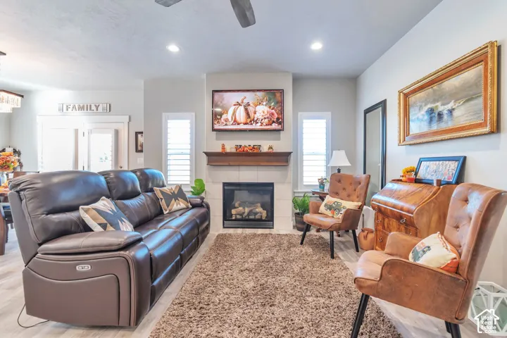 Fireplace with a wood mantel and tile surround, flanked by two windows with plantation shutters, recessed lighting, and a ceiling fan
