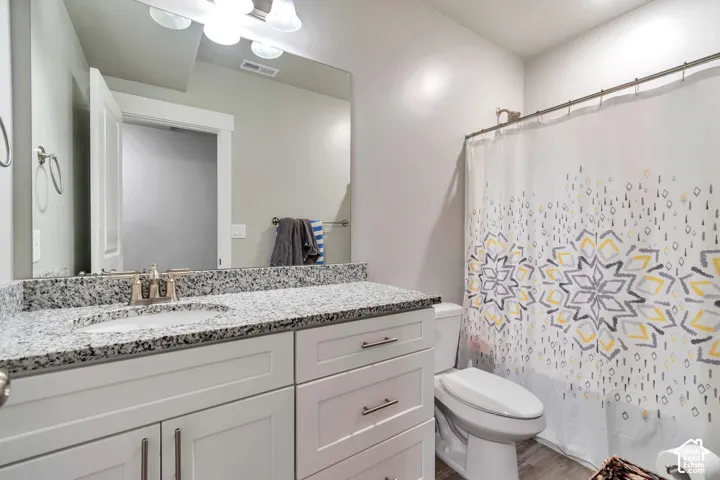 Bathroom featuring a white vanity cabinet with shaker-style doors, a speckled stone-finish countertop, an integrated oval sink, and a full-width wall mirror with attached multi-bulb lighting