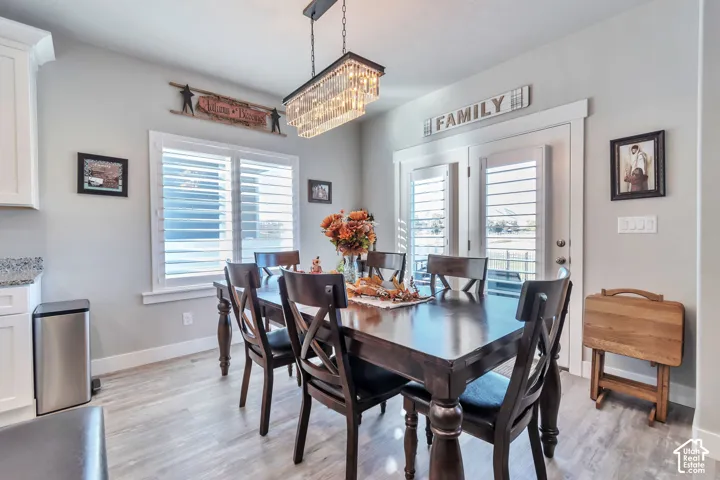 Dining area featuring wood-finish flooring, a rectangular multi-light tiered chandelier, white plantation shutters, and glass-paned doors