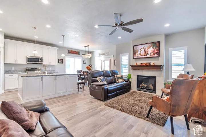 Open-concept kitchen featuring white shaker-style cabinetry, an island with stone countertops, recessed lighting, wood-finish flooring, and a fireplace with a wood mantel