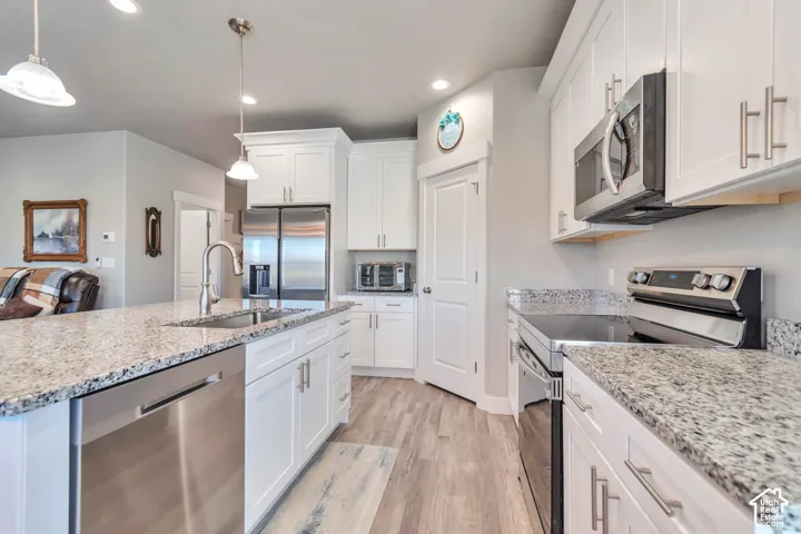 Kitchen featuring white cabinetry, stone countertops, stainless steel appliances, wood-finish flooring, and pendant lighting