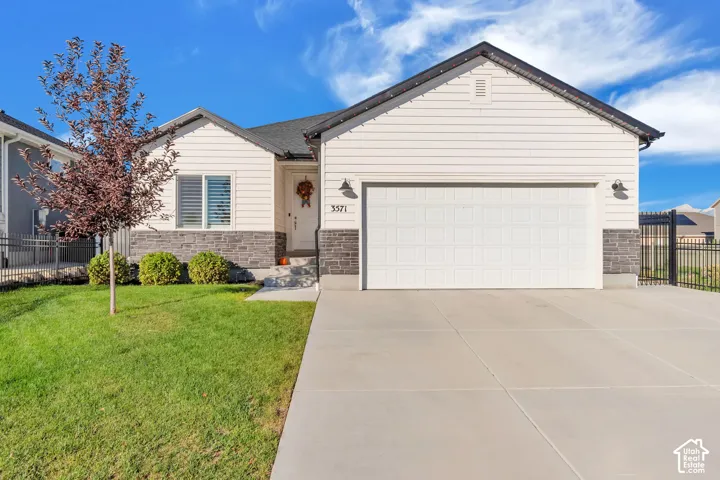 Single-story exterior featuring horizontal siding, stone veneer accents, an attached two-car garage, and perimeter metal fencing