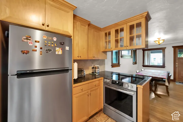 Kitchen featuring natural wood cabinetry, upper cabinets with glass-panel doors, dark stone-surface countertops, and stainless steel appliances