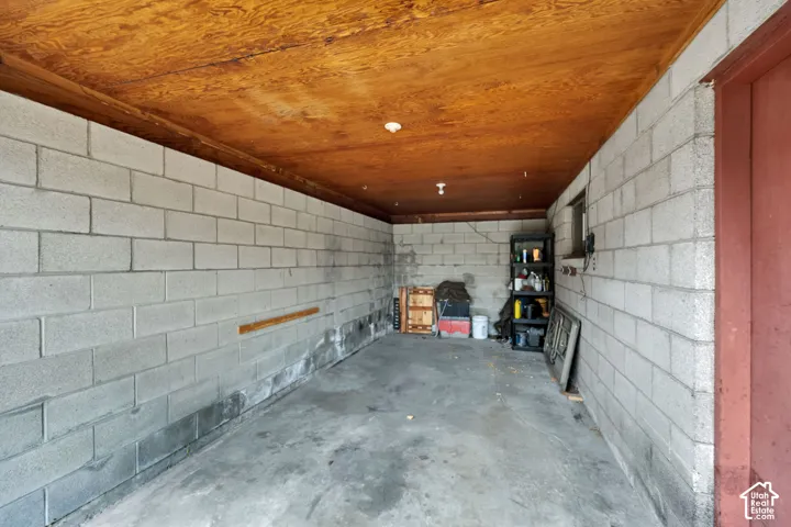 Enclosed storage area featuring concrete block walls, wood-paneled ceiling, and concrete flooring