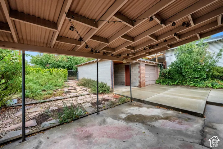 Covered patio featuring an exposed-beam ceiling and concrete flooring, complemented by an attached block-construction garage and irregular stone pathing
