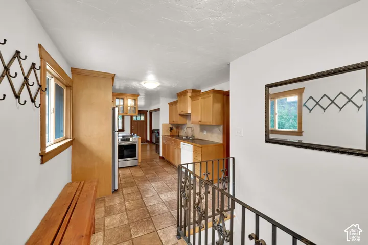 Kitchen area featuring wood cabinetry, stone-finish floor tiling, stainless steel appliance, and decorative iron railing