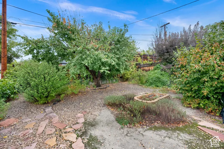 Backyard featuring mature trees, a stone pathway, gravel ground cover, and a brick-lined garden bed