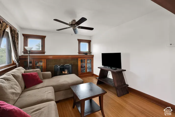 Living area featuring wood-finish flooring, a tile-surround fireplace, built-in cabinetry, and a ceiling fan