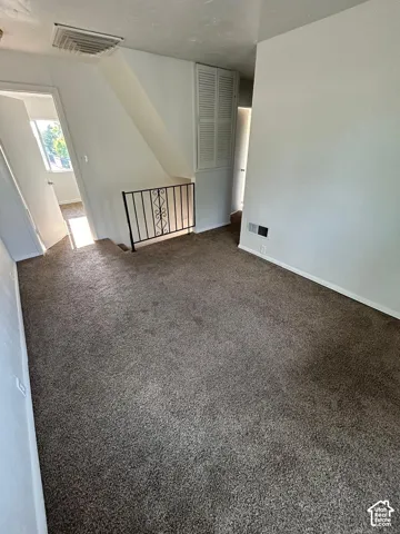 Carpeted room featuring integrated floor-to-ceiling louvered storage cabinetry and decorative metal stair railing