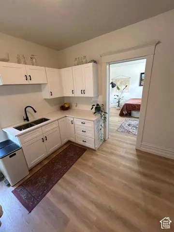 White shaker-style cabinetry, solid-surface countertops, dual-basin stainless steel sink with matte black fixture, and wood-finish flooring