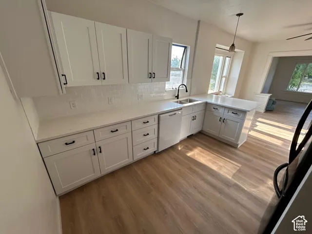 Kitchen featuring white shaker-style cabinetry, light-toned stone countertops, subway tile backsplash, matte black hardware, and wood-finish flooring