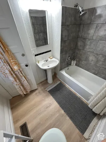 Bathroom featuring wood-finish flooring, a white pedestal sink, and a tub with a grey tile surround